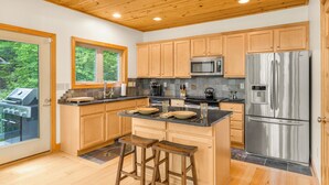 Une cuisine moderne avec des meubles en bois, des appareils en acier inoxydable et un coin bar avec des tabourets.