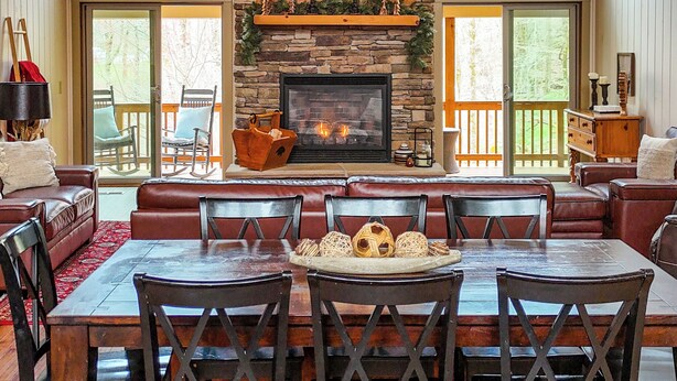 A spacious living room with a stone fireplace, wooden ceiling, and large windows. - Huge Decks, Hot Tub, Fire Pit & Dog Friendly. Close to Boone and Banner Elk. (Seven Devils)