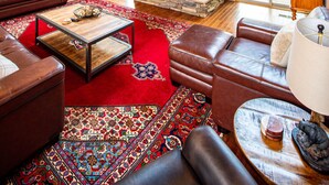 A spacious living room with a stone fireplace, leather furniture, and a high ceiling with wooden beams. - Huge Decks, Hot Tub, Fire Pit & Dog Friendly. Close to Boone and Banner Elk. (Seven Devils)