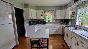 A modern kitchen with white cabinets, a marble countertop, a sink, a stove, and a window with a view of greenery. - Riverfront / Fishing / Elk Rail Trails / 4-bedroom house in beautiful Duck (Duck)