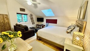 A bedroom with a bed, a desk, a chair, a TV, a ceiling fan, and a skylight.