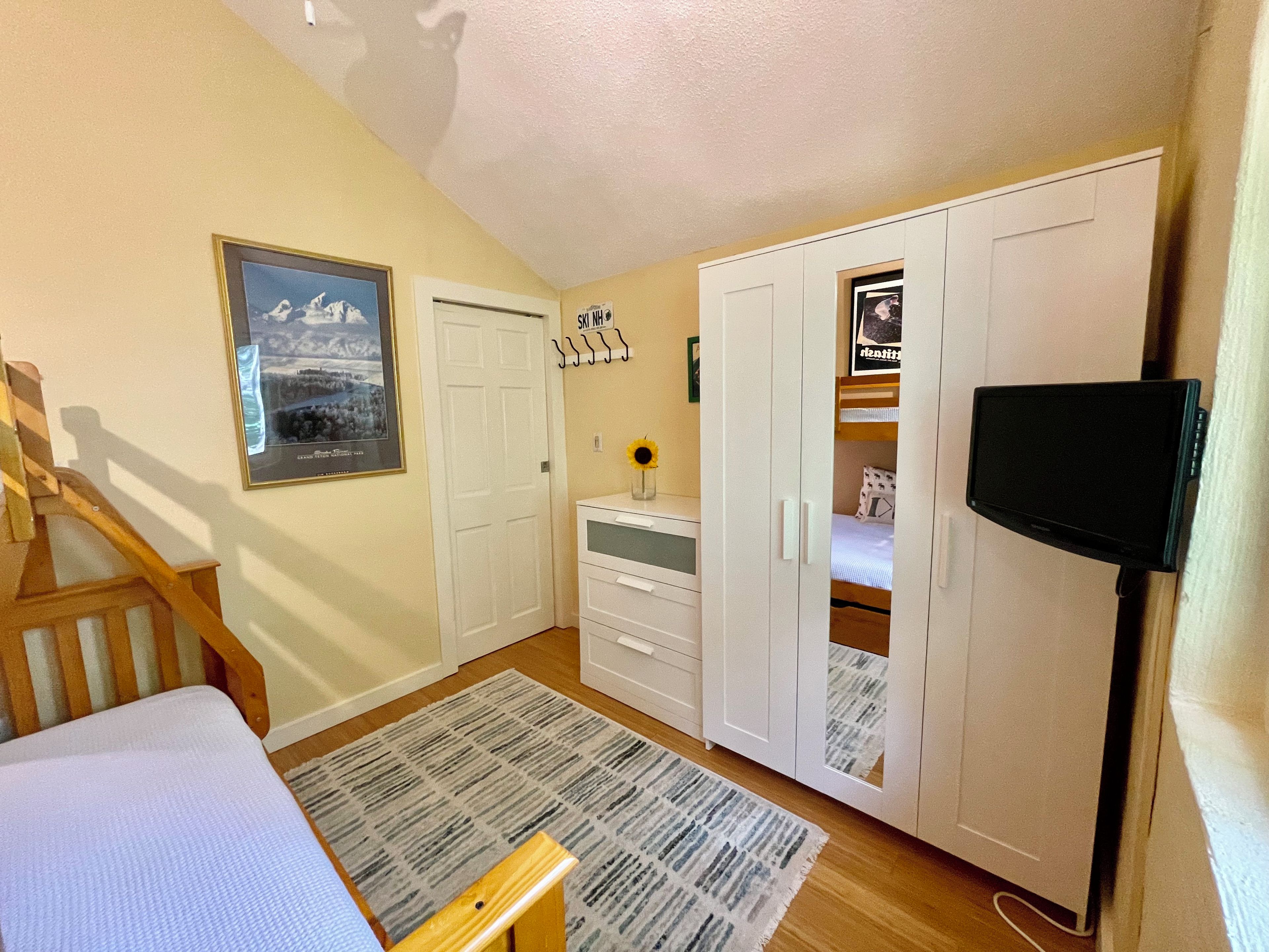 A bedroom with a bed, a desk, a wardrobe, and a television.