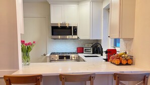 A kitchen with white cabinets, a central island with chairs, a microwave, a toaster, and a fruit basket.
