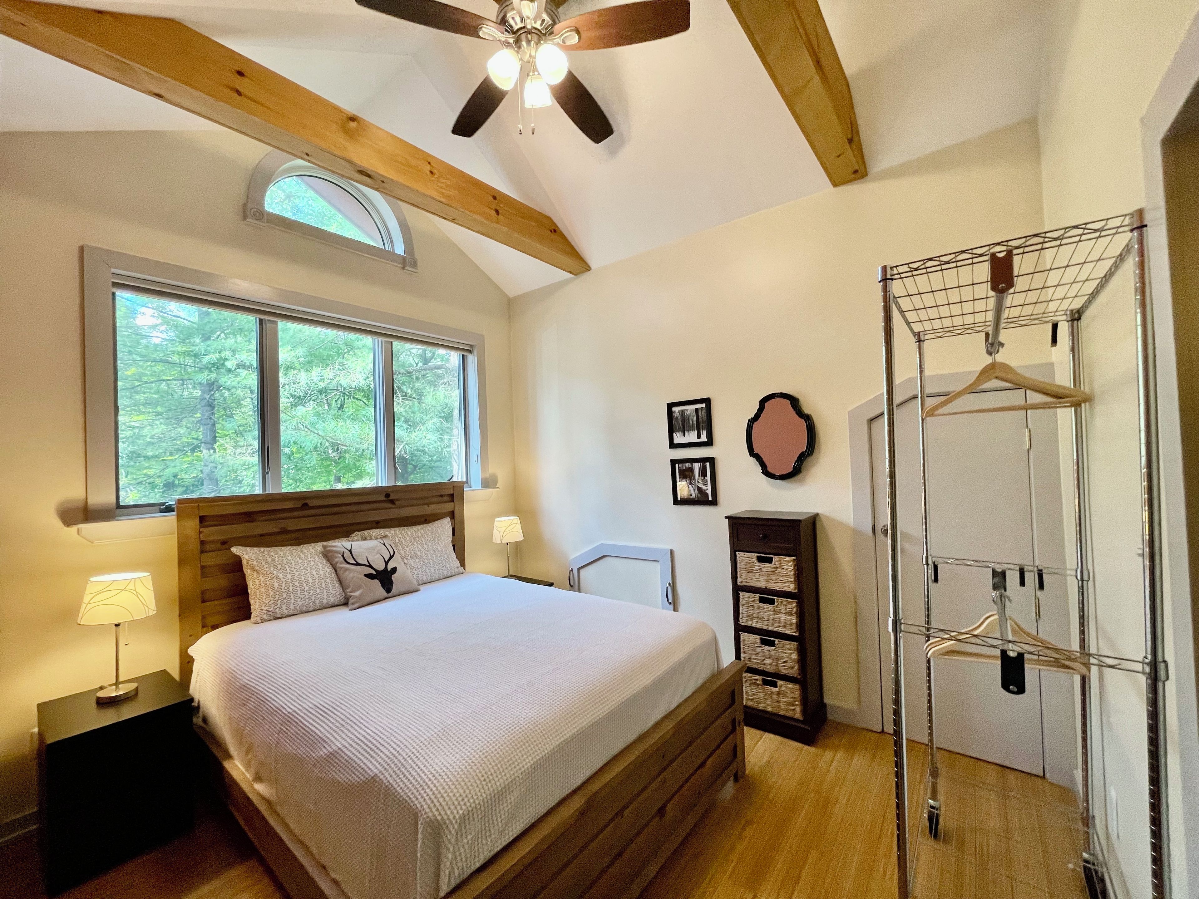 Une chambre à coucher comprenant un lit, un ventilateur de plafond, une fenêtre, une étagère fixée au mur et une tête de lit en bois.