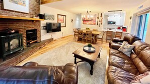 A spacious living room with a fireplace, leather sofa, dining area, and kitchen in the background.