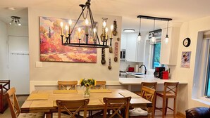A dining area with a wooden table and chairs, a chandelier, and a painting on the wall.