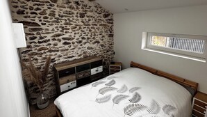 A bedroom with a skylight, stone wall, wooden bed frame, and a window with blinds.