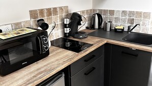 A compact kitchen with a microwave, coffee maker, kettle, and a small refrigerator.