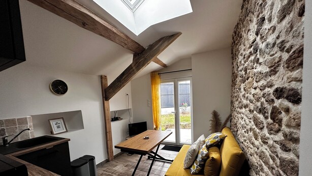 A compact kitchen with a wooden table, a yellow sofa, and a stone wall.