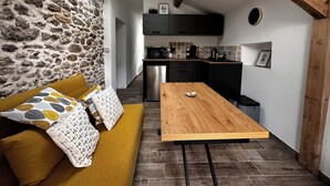 A compact living space with a stone wall, a wooden dining table, a mustard-colored sofa, and a kitchen area with modern appliances.