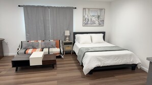 Ein Schlafzimmer mit einem Bett, einem Schlafsofa, einem Nachttisch, einer Lampe und einem Bild an der Wand.