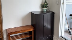 Ein Zimmer mit einer Holzbank, einem dunklen Schrank, einem an der Wand befestigten Kleiderhaken und einem kleinen Blumentopf.