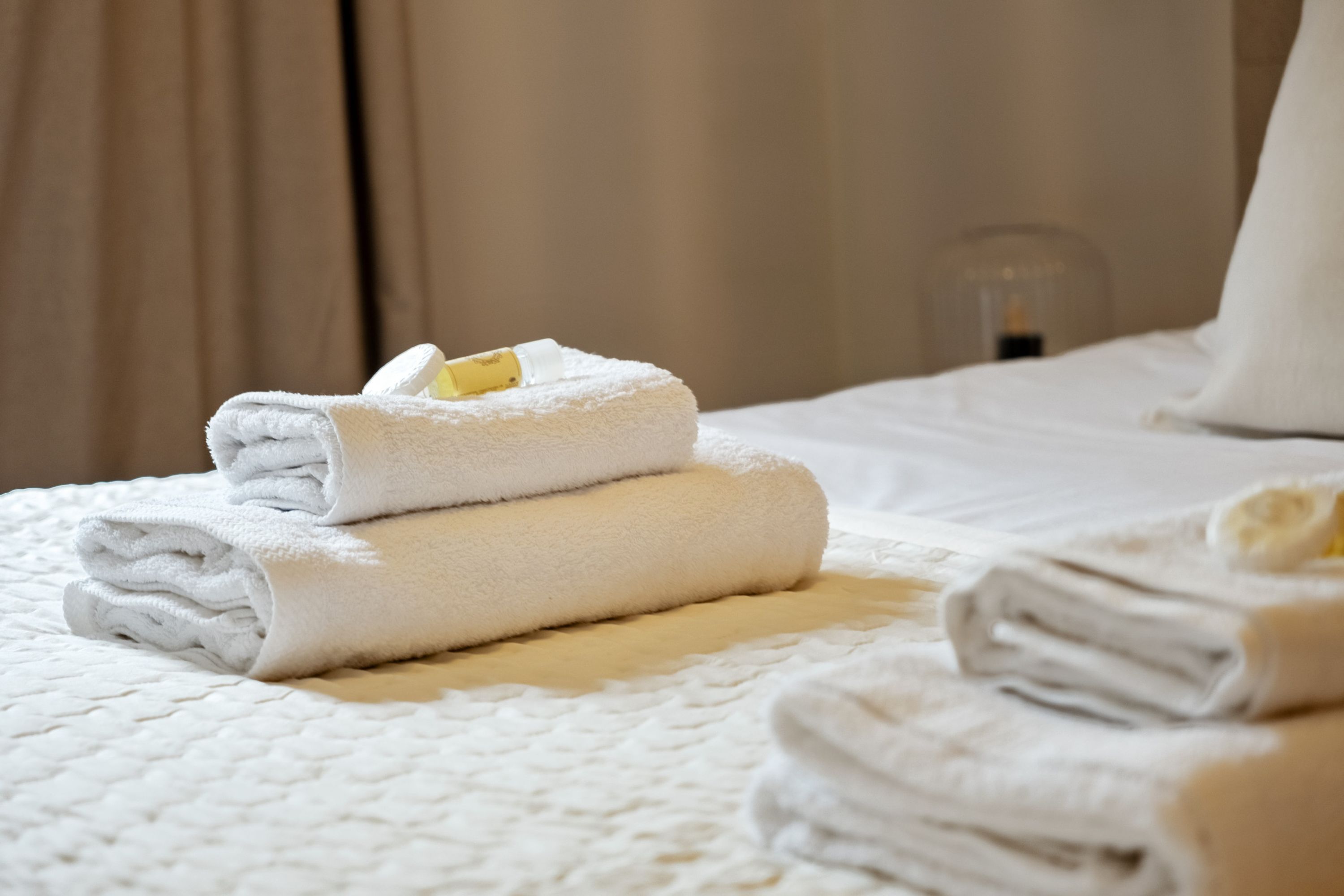 A neatly made bed with folded white towels and a yellow object on top.