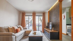 A modern living room with a sofa, coffee table, TV, and kitchen area. - Urban Stay 1A by Homie (Funchal)