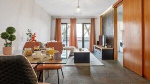 A modern living room with a glass dining table, comfortable seating, a TV, and a view of the outdoors. - Urban Stay 1A by Homie (Funchal)