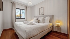 A modern hotel room with a large bed, a bedside table with a lamp, and a window with curtains. - Urban Stay 1A by Homie (Funchal)