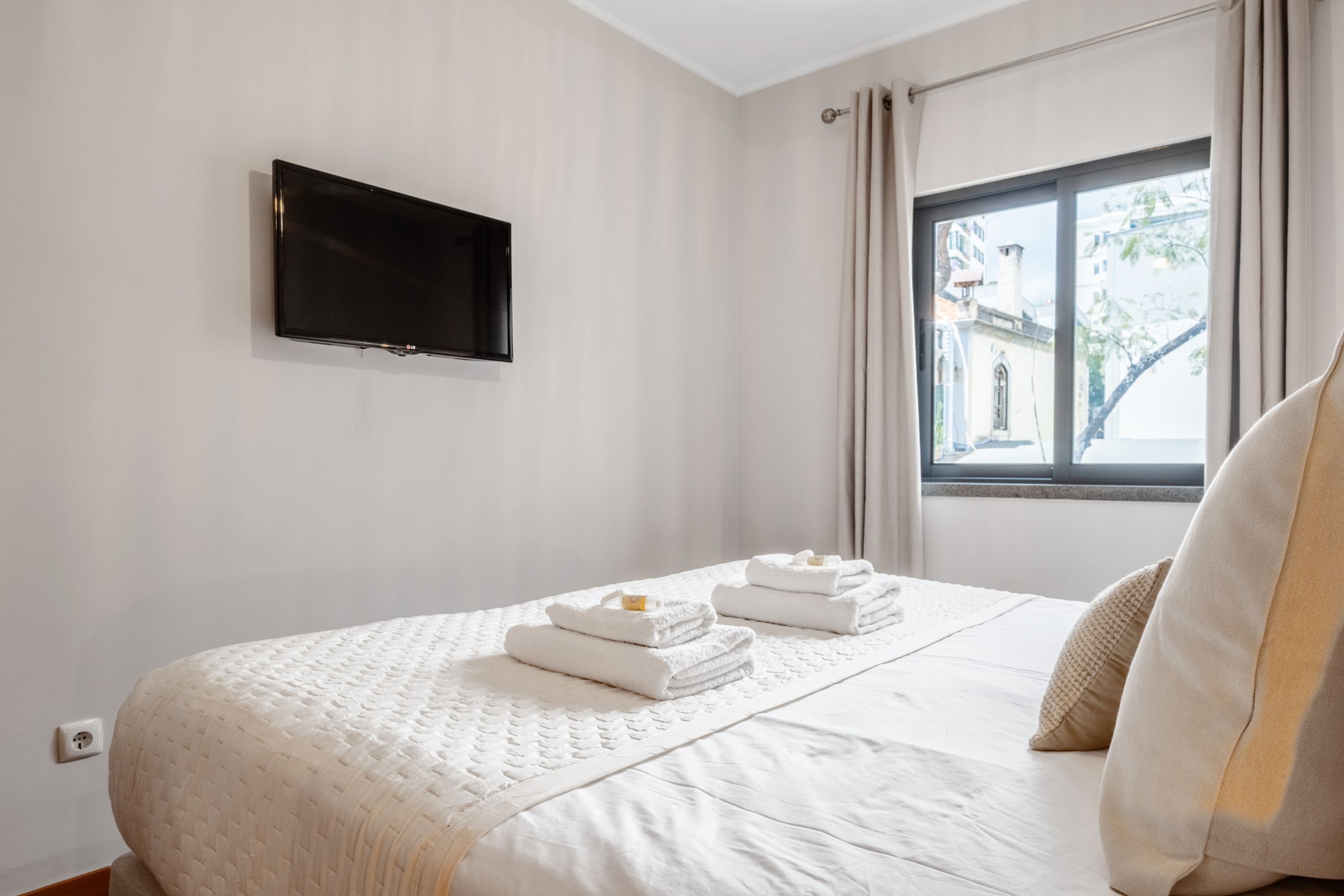 Hotellihuone, jossa on sänky, taulutelevisio ja ikkuna, jossa on verhot.
