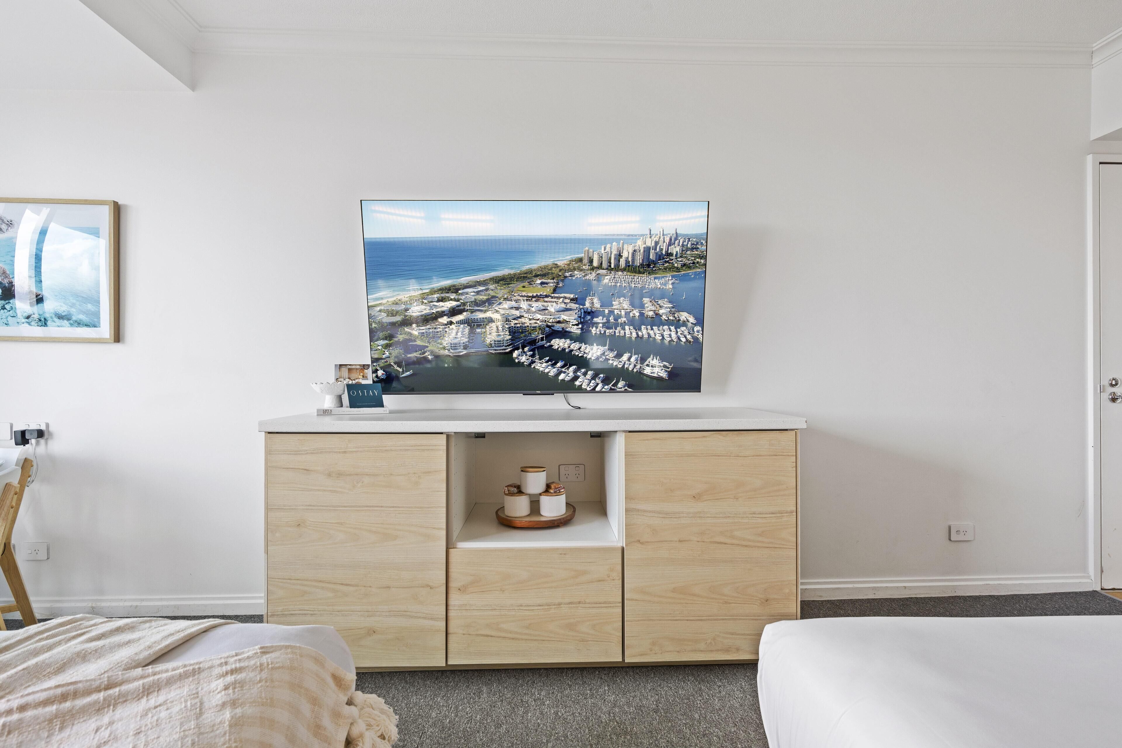 Une chambre d’hôtel dotée d’un grand téléviseur à écran plat fixé au mur blanc, d’un meuble en bois en dessous et d’un lit recouvert d’une couette blanche.