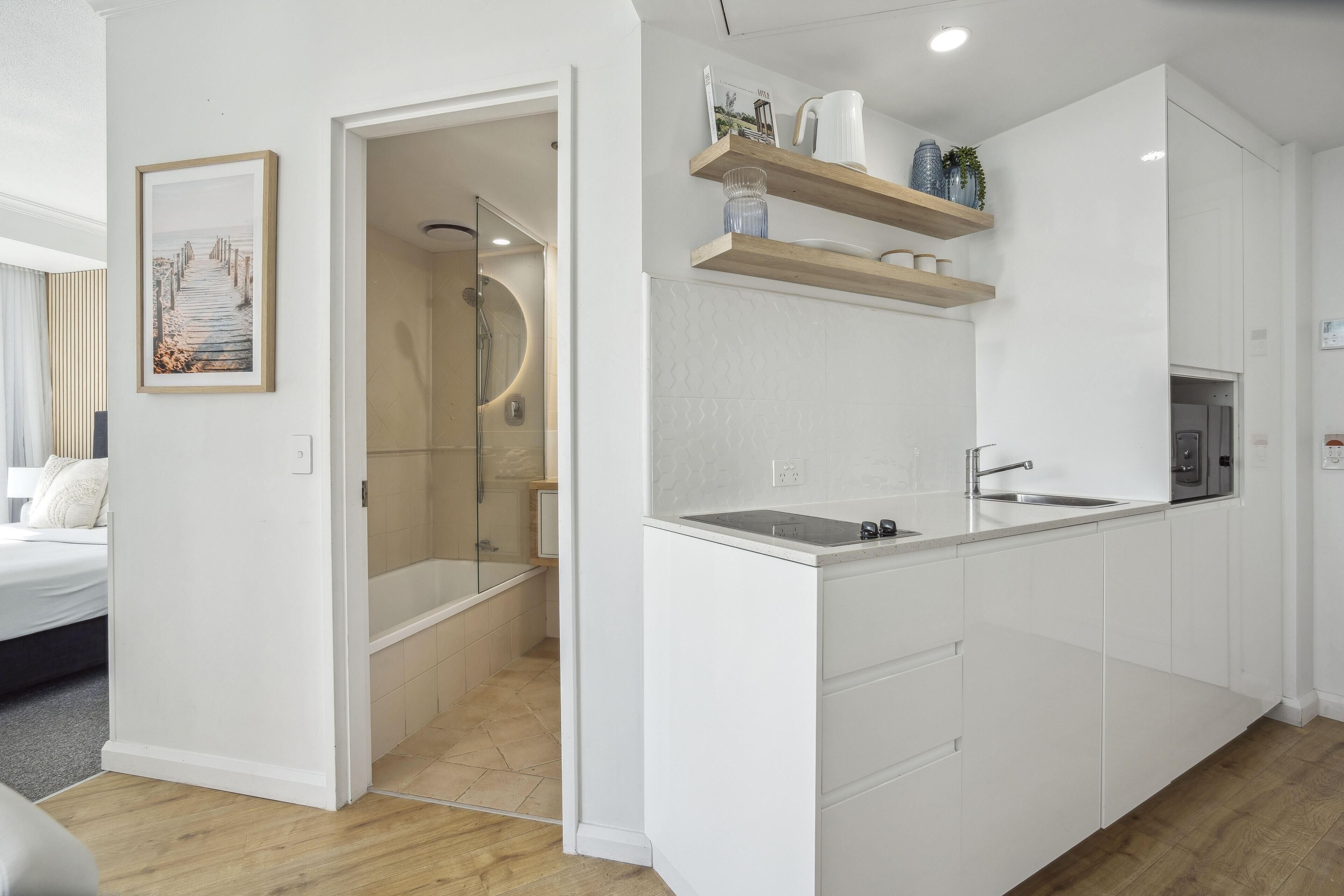 Une cuisine moderne avec des meubles blancs, un lave-vaisselle encastré et des étagères en bois au-dessus du plan de travail.