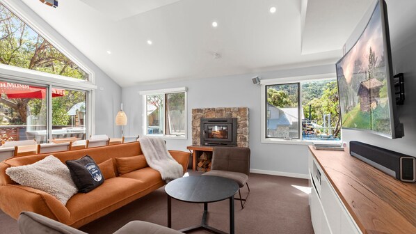 A modern living room with a stone fireplace, large windows, and a cozy seating area.