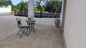 Eine Terrasse mit zwei Metallstühlen und einem Tisch, einer großen Vase und einer Steinmauer im Hintergrund.