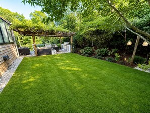 A well-maintained backyard with a wooden pergola, outdoor seating, and a grill area.