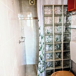 Une salle de bain avec des carreaux blancs, une douche en verre et un mur carrelé orné d’un motif en bambou.