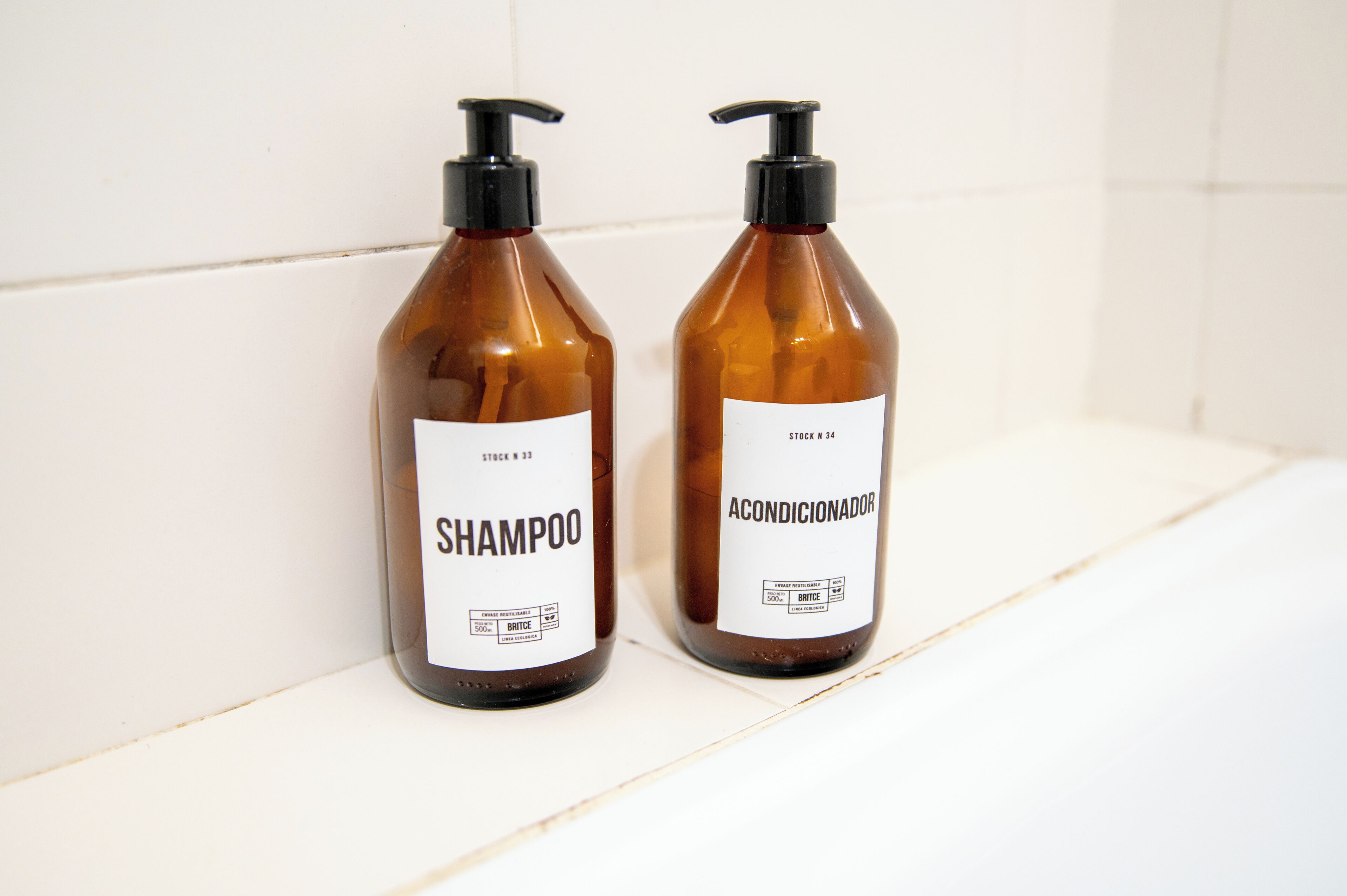 Dos botellas de champú y acondicionador sobre un estante blanco.