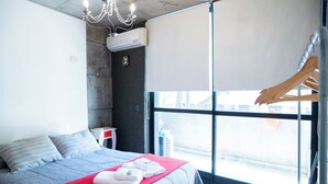 A modern hotel room with a large bed, a red blanket, and a view through a window. - Charming studio in beautiful Buenos Aires with AC, WiFi (Buenos Aires)