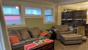 A living room with a brown leather sofa, a brown leather armchair, and a wooden coffee table with a colorful throw. - Charming 1916 Craftsman Near UNC & Historic Downtown Greeley with AC and WiFi (Greeley)