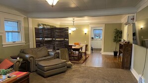 A living room with a sofa, a coffee table, and a dining area with a table and chairs. - Charming 1916 Craftsman Near UNC & Historic Downtown Greeley with AC and WiFi (Greeley)