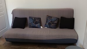 A sofa with a patterned cover and two decorative pillows, a small round table, and a wooden floor. - Quiet country gite with air conditioning.  (Aups)
