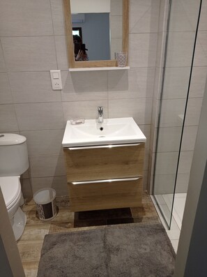 A bathroom with a white sink, wooden vanity, and a glass shower enclosure.