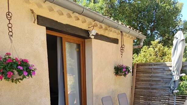 An outdoor patio with a table and chairs, a wooden fence, and hanging flower baskets. - Quiet country gite with air conditioning.  (Aups)