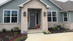 A two-story house with a brick facade, a front porch, and a small garden with flowers and shrubs. - Quiet 4BR 2.5BA Modern New Country Home in Weatherford (Weatherford)