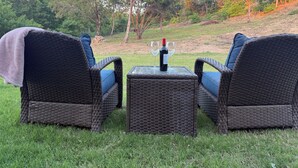 Two wicker chairs with blue cushions and a small table with a bottle and glasses, set on a grassy lawn with trees in the background. - Quiet 4BR 2.5BA Modern New Country Home in Weatherford (Weatherford)