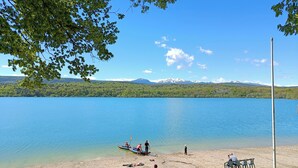 A lakeside view with a sandy beach, kayaks, and people.