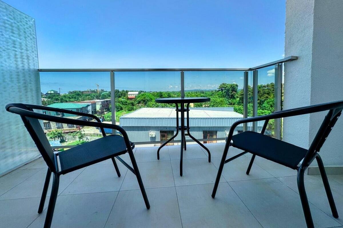 A balcony with two chairs and a small table, overlooking a residential area with houses and greenery.