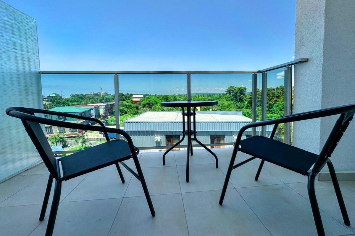 A balcony with two chairs and a small table, overlooking a residential area with houses and greenery.