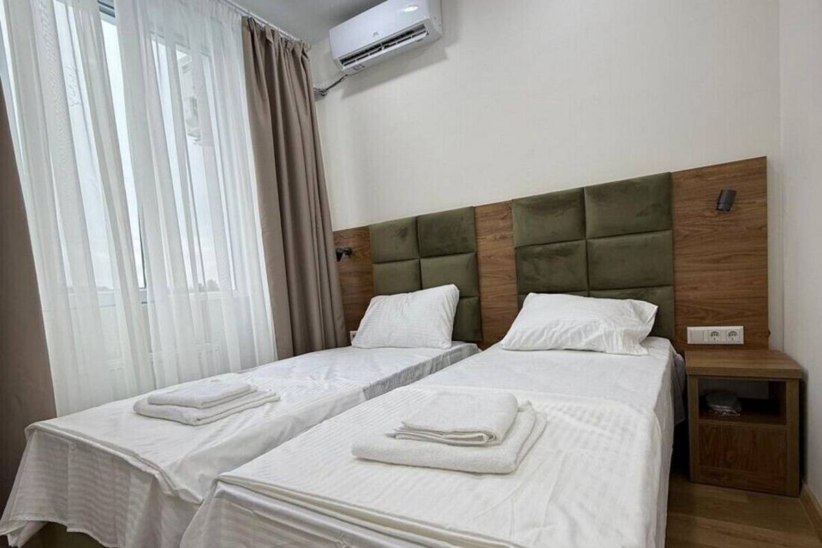 A hotel room with two beds, a wooden headboard, a nightstand, and an air conditioning unit.
