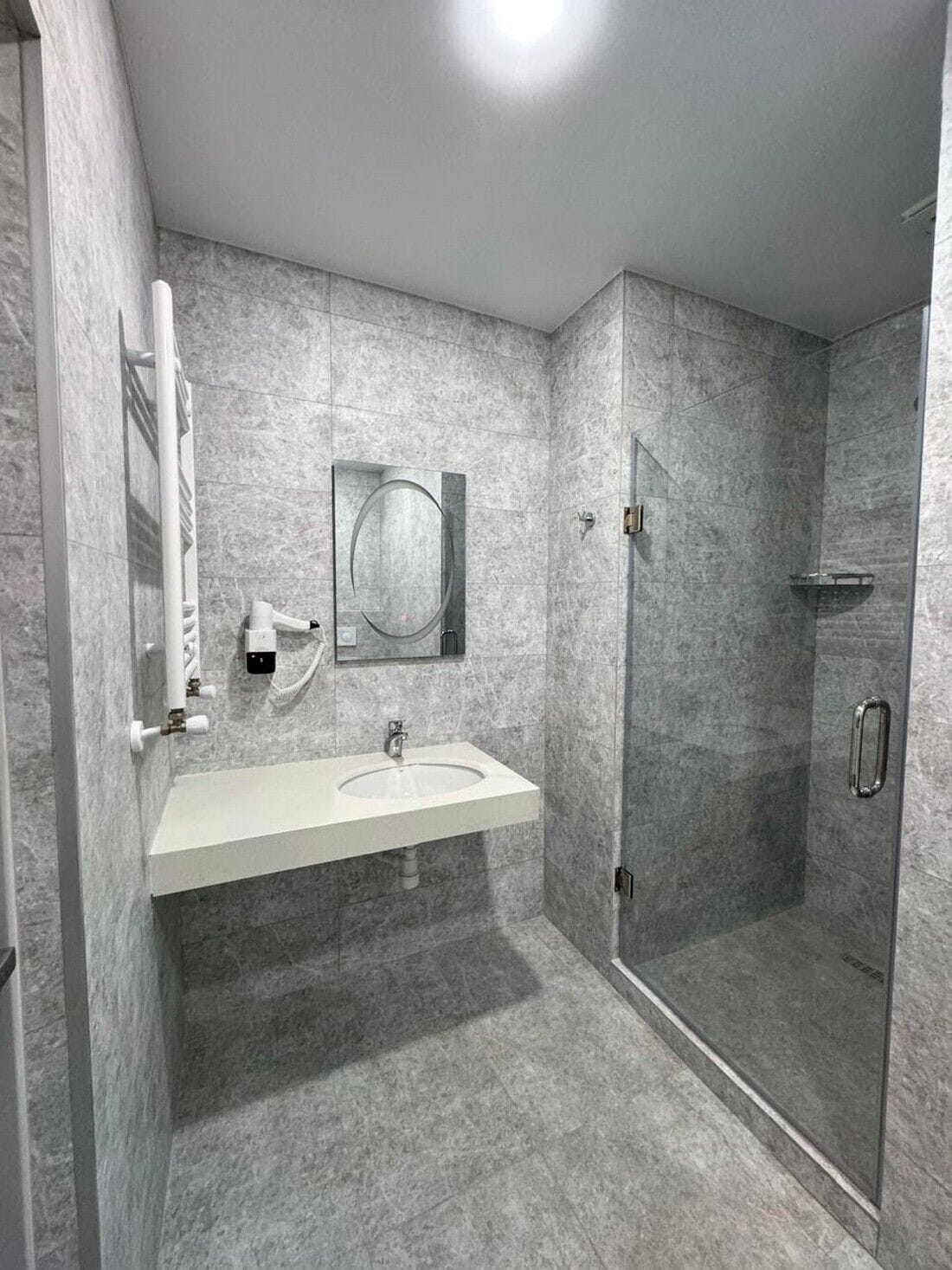 A modern bathroom with a marble sink, a glass-enclosed shower, and a wall-mounted mirror.