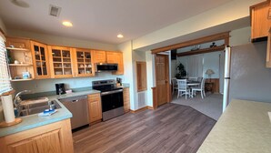 A kitchen with wooden cabinets, stainless steel appliances, and a dining area with a table and chairs. - Charming Sound-front Captains Quarters in Frisco WiFi, streaming & perfect views (Frisco)