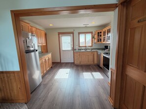A kitchen with wooden cabinets, a refrigerator, a sink, and a window with blinds.