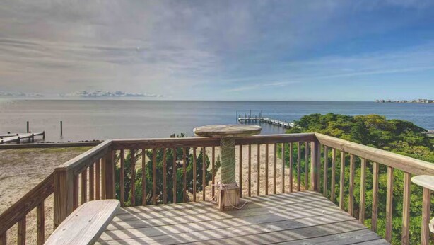 A wooden deck with a stone table, overlooking a beach and a pier extending into calm waters. - Charming Sound-front Captains Quarters in Frisco WiFi, streaming & perfect views (Frisco)