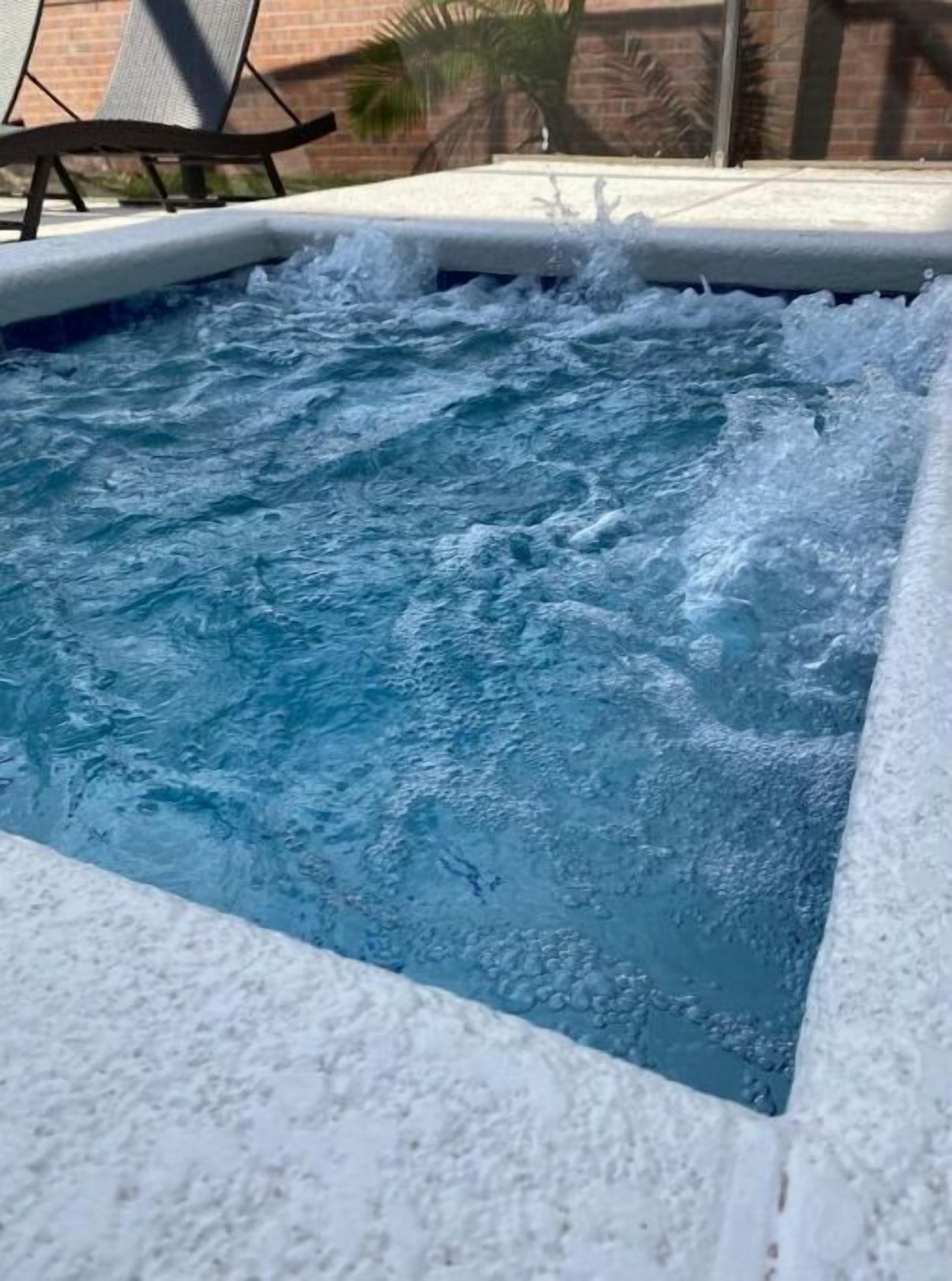 A hot tub with water jets, surrounded by a white pool edge and a brick wall in the background.