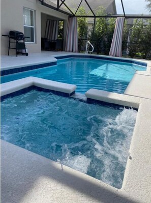 Una piscina con zona de hidromasaje, rodeada por un porche cubierto con vistas a zonas verdes.