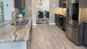 Una cocina moderna con refrigerador de acero inoxidable, encimera de mármol y comedor con candelabro.