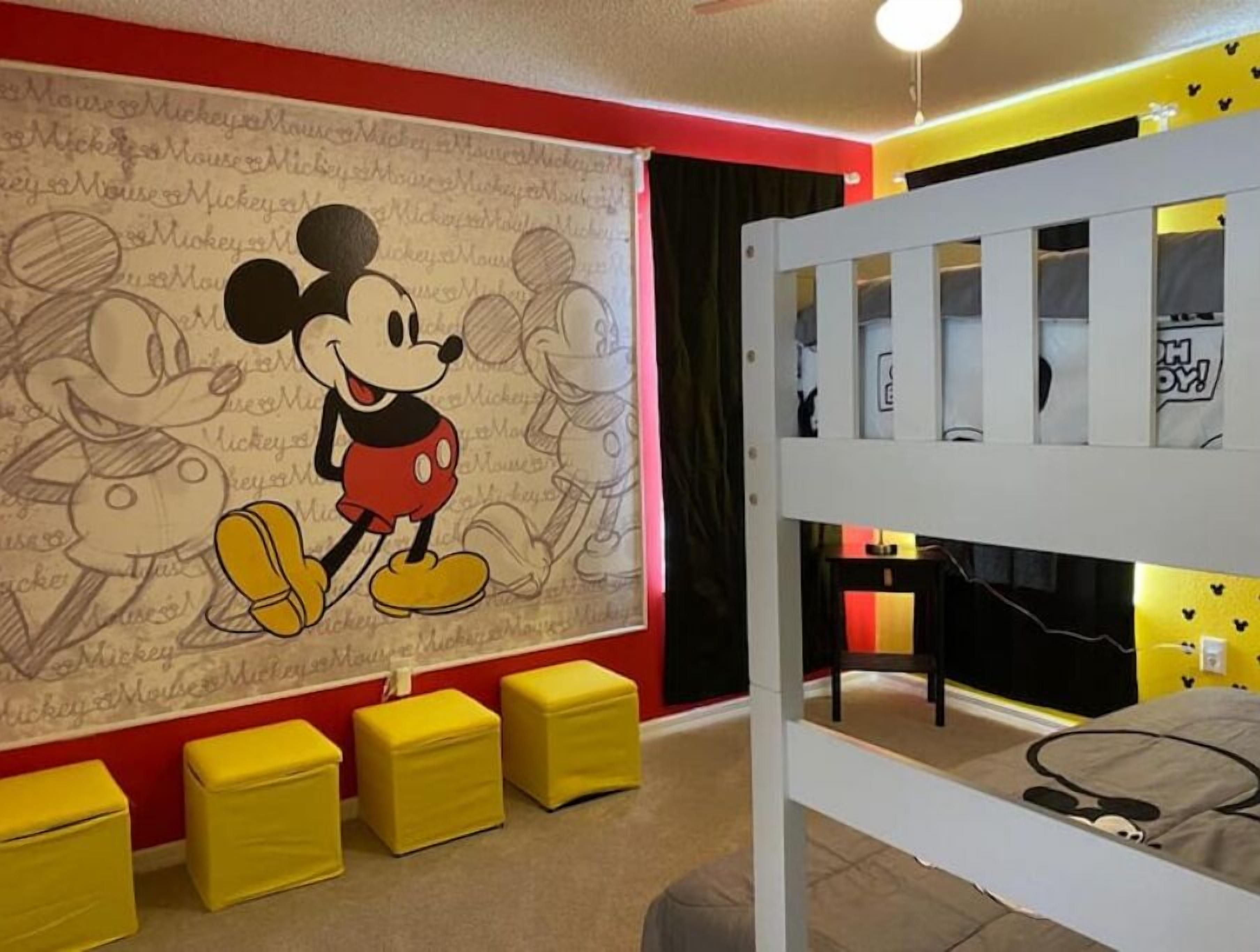 Una habitació amb un mural gran de Mickey Mouse, una llitera i otomans grocs.