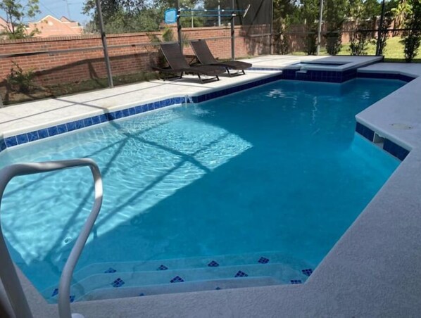 Una piscina con borde de azulejos, barandilla metálica y pared de ladrillo al fondo.