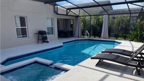 Una piscina con un porche de vidrio, una silla de descanso y una mesa.